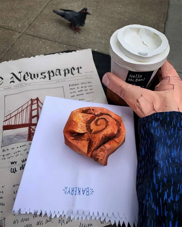 Paper sculpture of a person holding a coffee cup and a cinnamon roll and newspaper on a table with a pigeon looking on.. Illustration by Dan Bransfield, Lifestyle, Whimsical, 